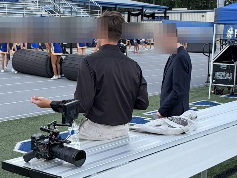 Sideline camera and student reporter at a high school football game
